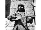 Instruments are played mainly to accompany the voice. This boy, with fingers protected by a plectrum, thrums monotonously on his primitive guitar, to enhance the simple melody of his song. An early photograph.